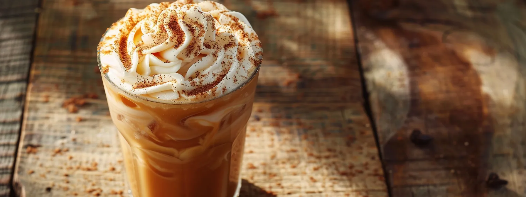 a glass filled with iced chai latte, topped with a swirl of whipped cream and a sprinkle of cinnamon, sitting on a rustic wooden table.