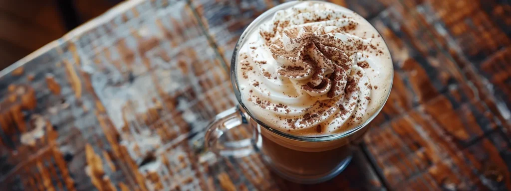 a creamy, chocolate latte topped with a generous swirl of whipped cream and sprinkled with cocoa powder, served in a clear glass mug on a rustic wooden table.